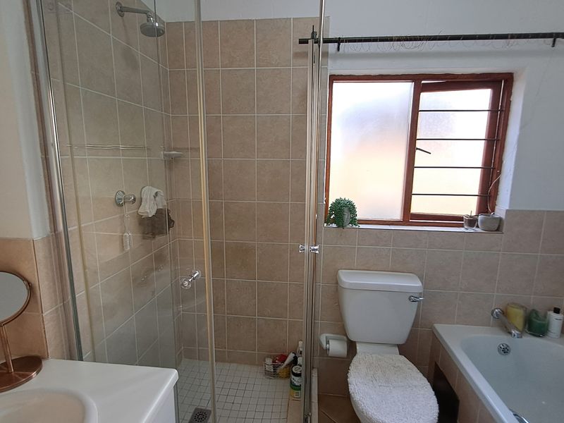A functional bathroom featuring a glass-enclosed shower, a standard bathtub, a toilet, and a vanity basin with neutral wall and floor tiling.