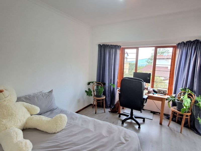 A bedroom featuring laminate flooring, timber window frames, and natural light, offering a functional space with views of the surrounding area.