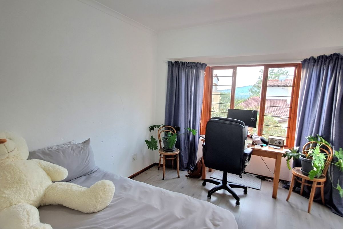 A bedroom featuring laminate flooring, timber window frames, and natural light, offering a functional space with views of the surrounding area.