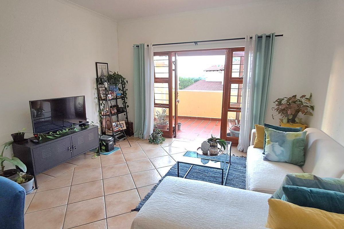 A bright living room featuring ceramic tile flooring and double doors opening onto a private balcony, providing natural light and outdoor access.