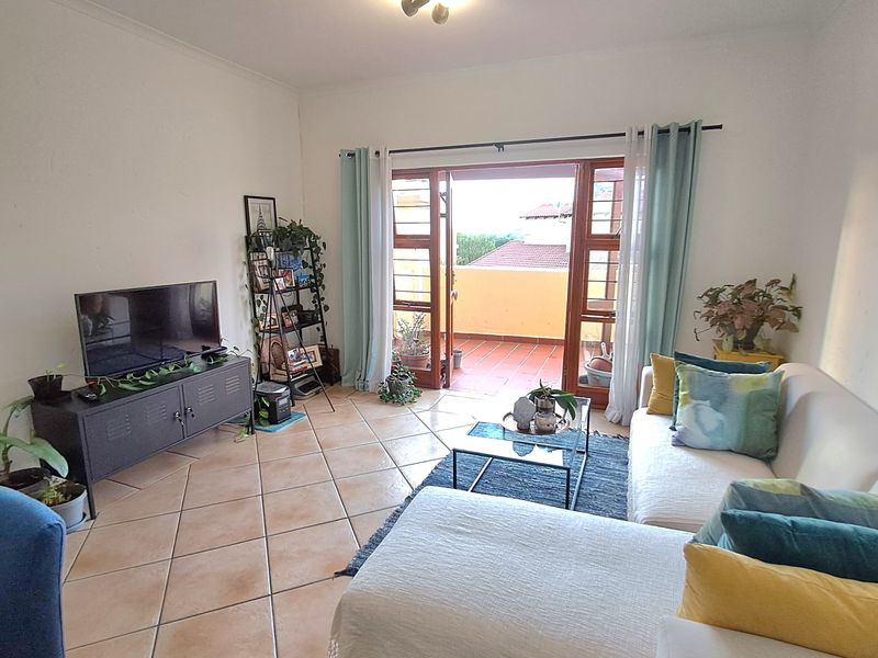 A bright living room featuring ceramic tile flooring and double doors opening onto a private balcony, providing natural light and outdoor access.