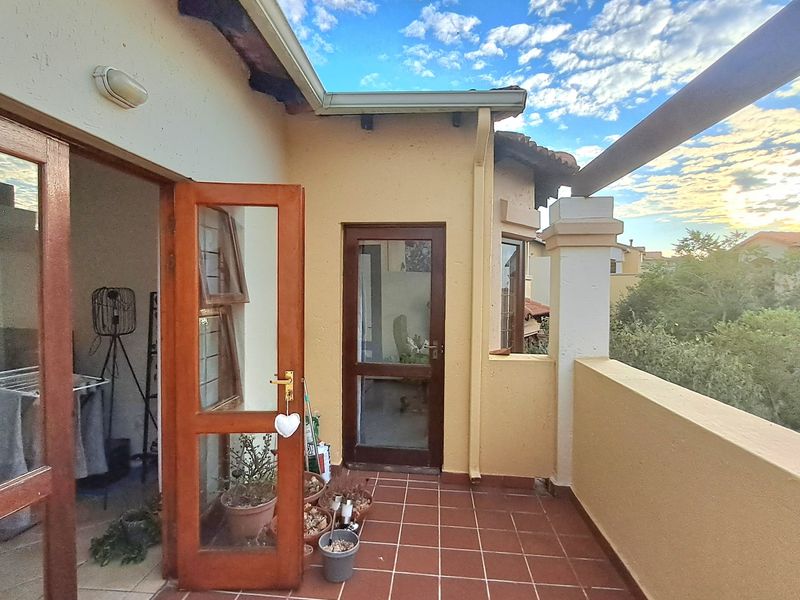 A tiled balcony area featuring wooden door frames and exterior wall lighting, offering an outdoor space accessible from the interior.