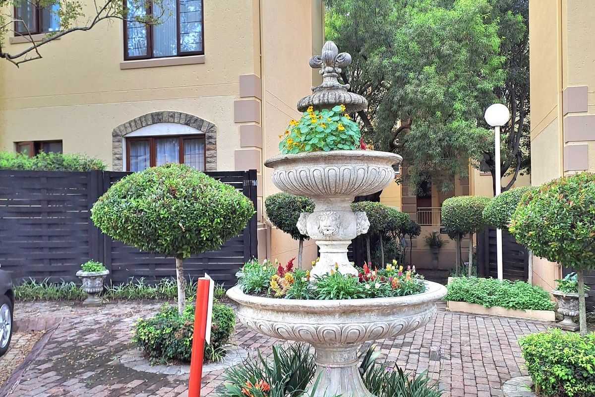 A well-maintained courtyard area featuring a decorative stone fountain, brick paving, and established landscaping between apartment building sections.