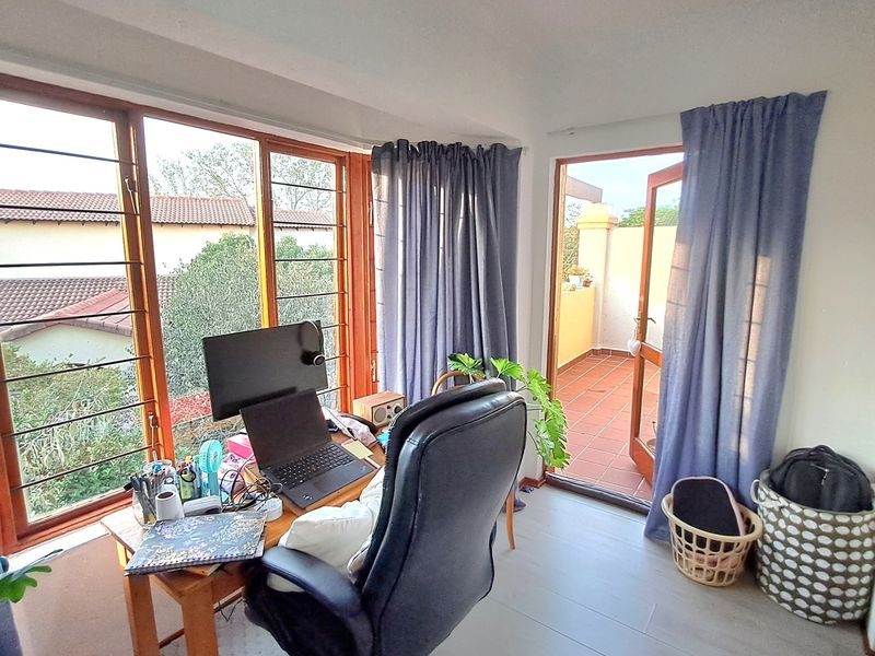 A bright home office space featuring large windows with natural light and direct access to an outdoor balcony area.