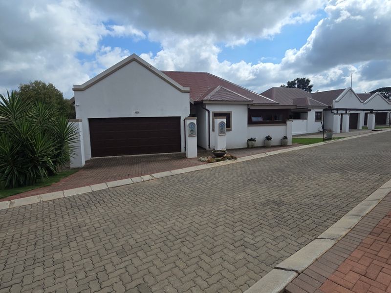Front elevation of a townhouse featuring a double garage, paved driveway, and well-maintained exterior finishes under a tiled roof.