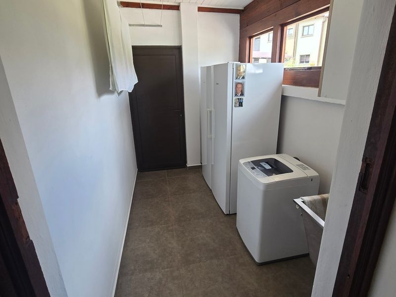 A functional laundry area featuring tiled flooring, exposed timber ceiling beams, and a practical ceiling-mounted drying rack.