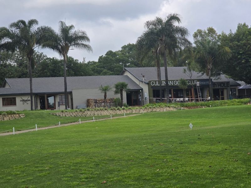 View of the rear elevation of the clubhouse building, featuring a tiled roof, covered patio area, and expansive landscaped lawn.