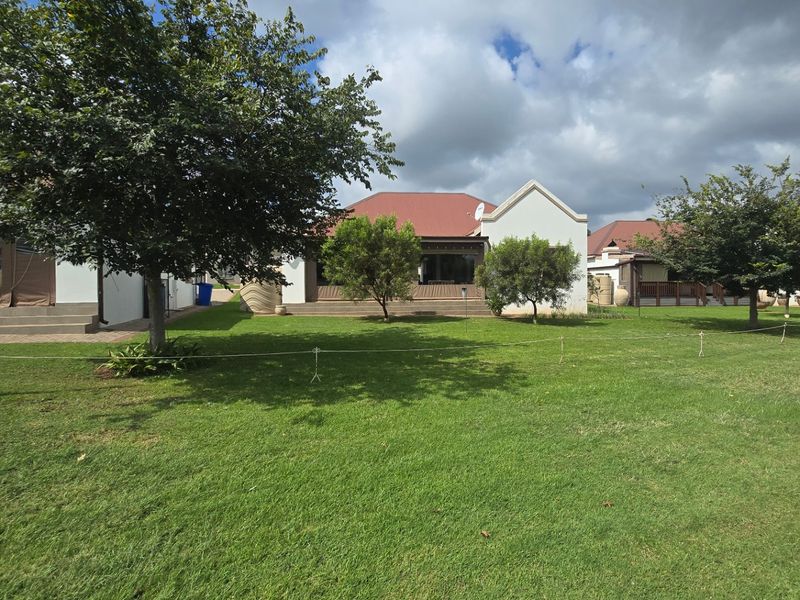 A view of the rear exterior of the townhouse, featuring a well-maintained lawn, a covered patio area, and a metal roof structure.