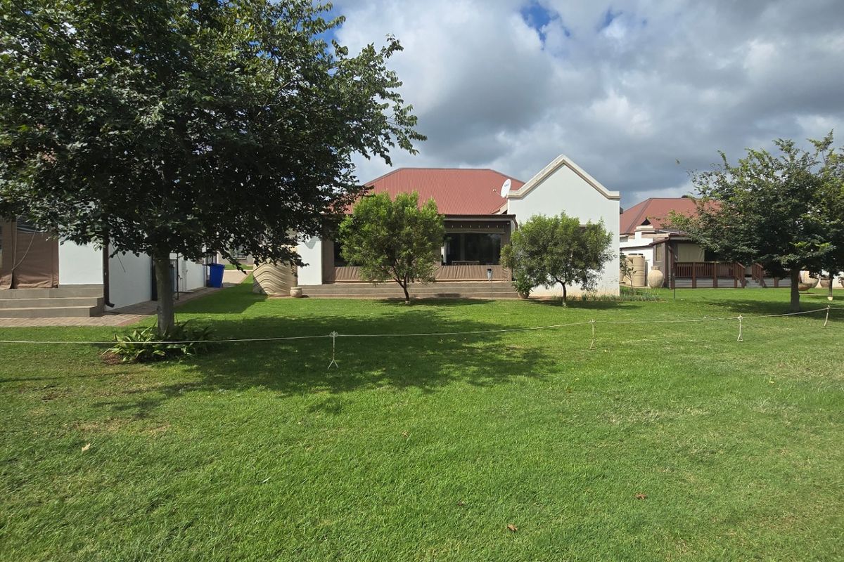 A view of the rear exterior of the townhouse, featuring a well-maintained lawn, a covered patio area, and a metal roof structure.
