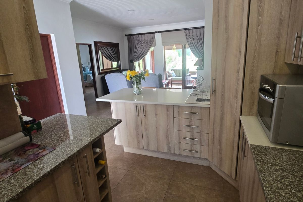 Modern kitchen featuring wood-look cabinetry, granite countertops, and a breakfast bar, flowing into an open-plan living area with tiled floors and a paneled ceiling.