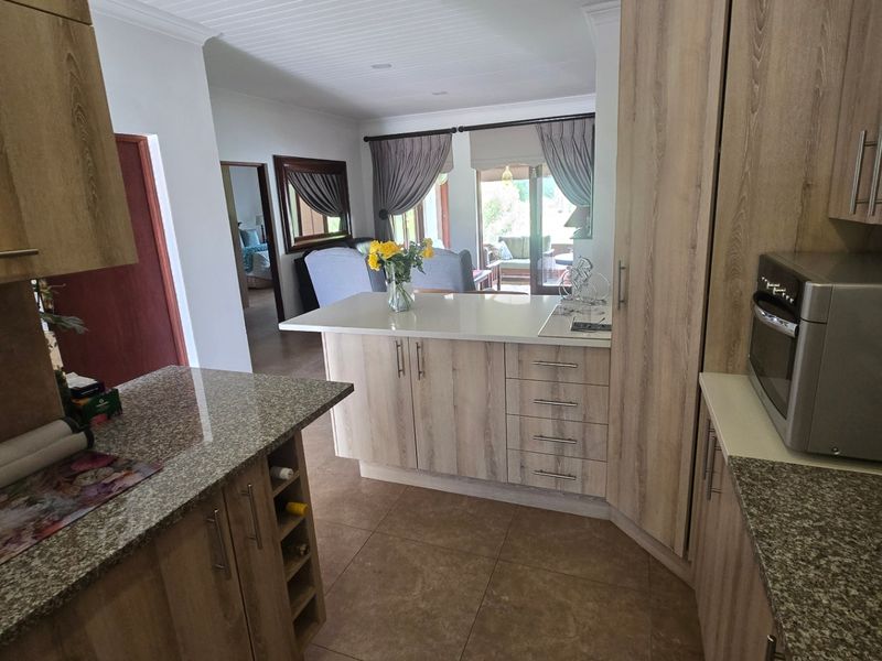 Modern kitchen featuring wood-look cabinetry, granite countertops, and a breakfast bar, flowing into an open-plan living area with tiled floors and a paneled ceiling.