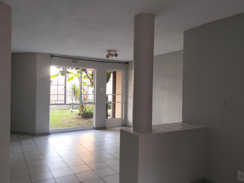 An empty, open-plan living area featuring tiled flooring, a structural column, and a tiled partition wall with direct access to the garden.