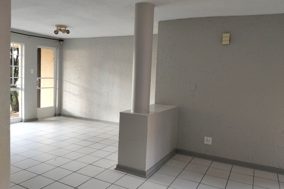 An empty, open-plan living area featuring neutral grey walls, white ceramic floor tiles, and a central structural column leading to an exterior door.