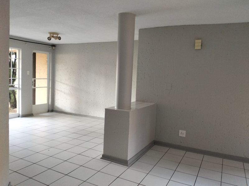 An empty, open-plan living area featuring neutral grey walls, white ceramic floor tiles, and a central structural column leading to an exterior door.