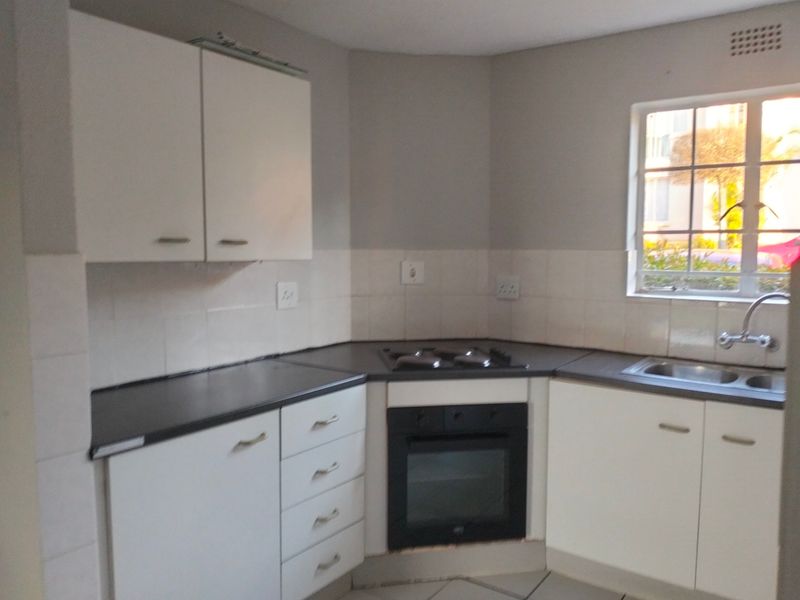 A functional kitchen featuring white cabinetry, dark countertops, a built-in oven with gas hob, and a stainless steel sink under a window.