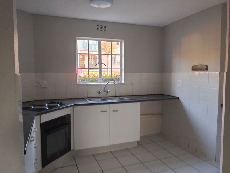 A functional kitchen featuring built-in cabinetry, an electric oven and hob, double sink, and tiled splashbacks with neutral tiled flooring.