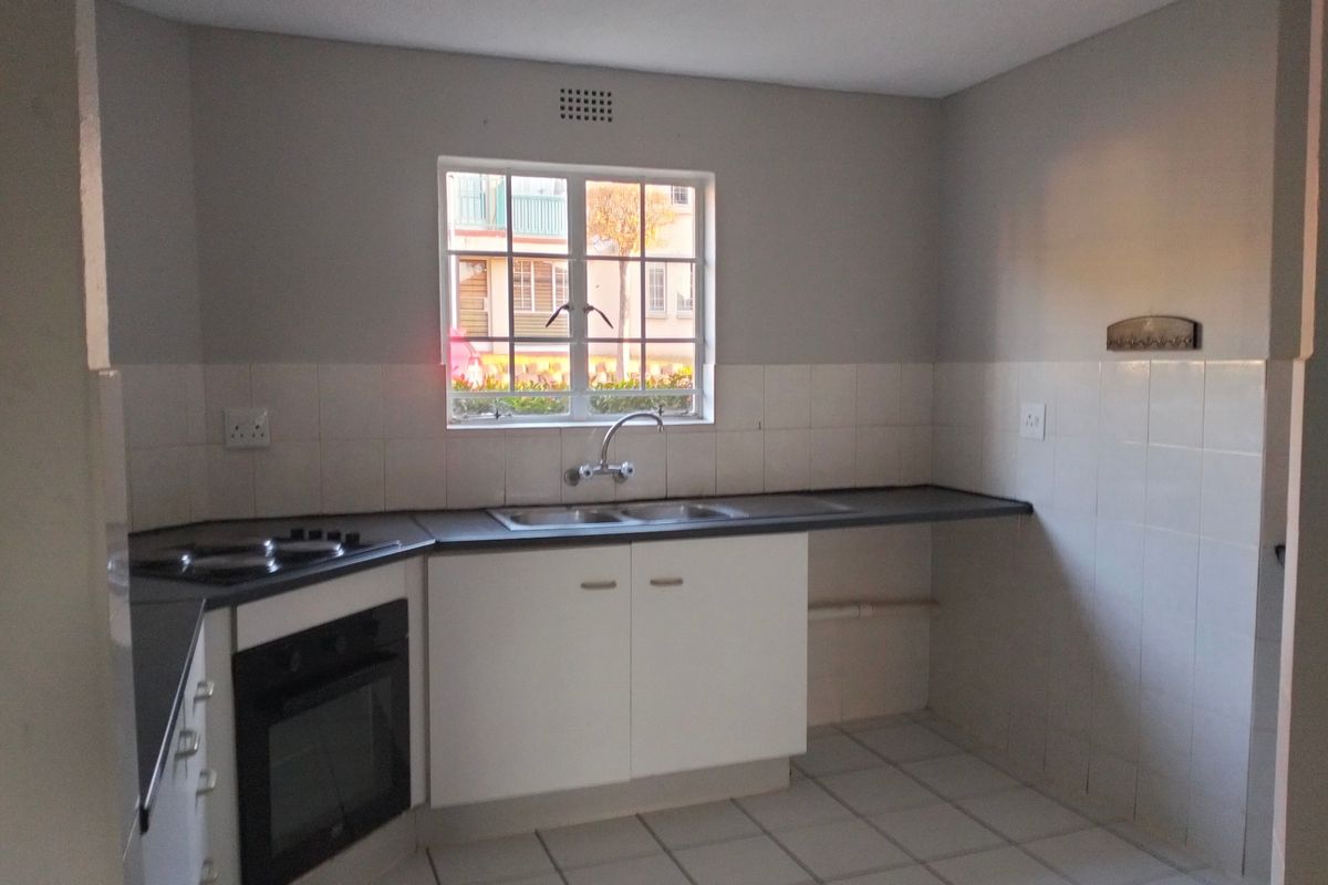 A functional kitchen featuring built-in cabinetry, an electric oven and hob, double sink, and tiled splashbacks with neutral tiled flooring.