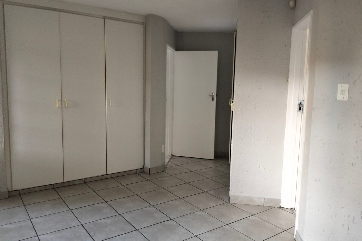 An empty bedroom featuring neutral tiled flooring and built-in cupboards, offering a blank canvas for personalization.