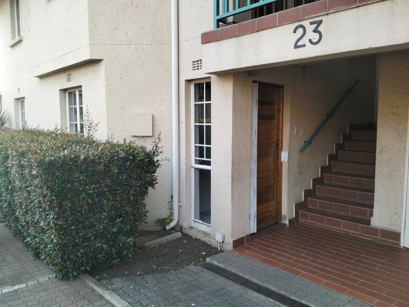 Exterior view of apartment unit 23, featuring a tiled entrance area, staircase with handrail, and timber front door.