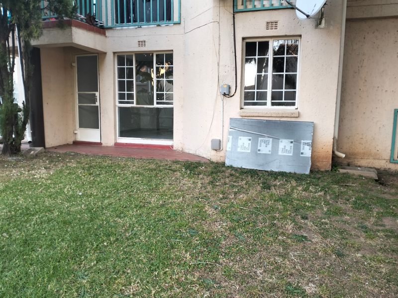 Rear view of the apartment building featuring a small garden area, security gate, and balcony access with visible exterior wall wear.