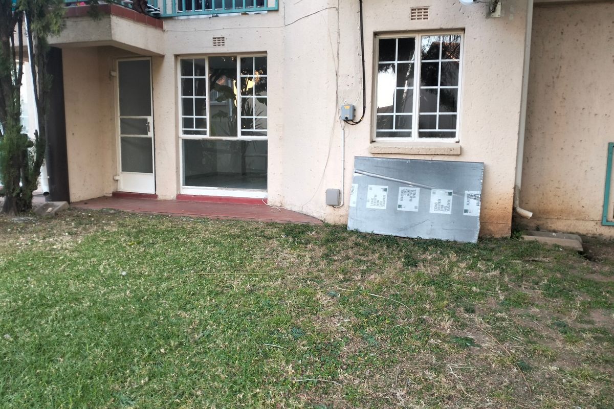 Rear view of the apartment building featuring a small garden area, security gate, and balcony access with visible exterior wall wear.