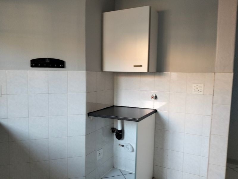 A functional laundry area featuring tiled splashbacks, a wall-mounted storage cabinet, and dedicated plumbing connections for an appliance.