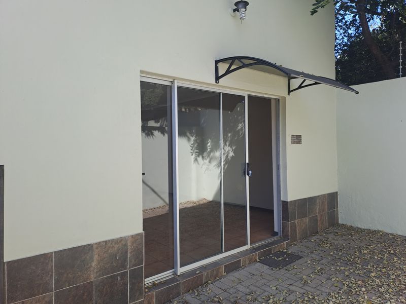 Rear exterior view of the townhouse featuring a sliding glass door, protective awning, and paved patio area.