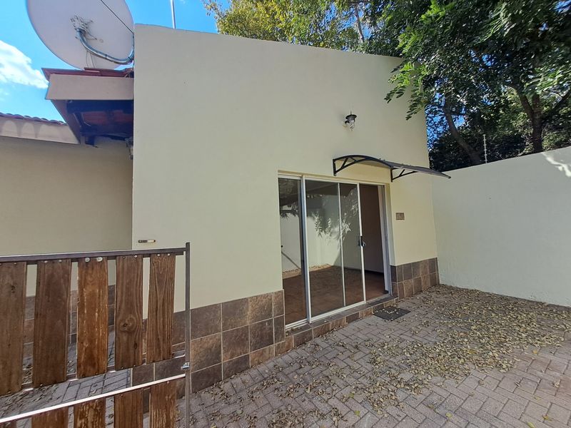 Rear exterior view of the townhouse featuring a paved patio area, sliding glass door access, and an exterior wall-mounted light fixture.