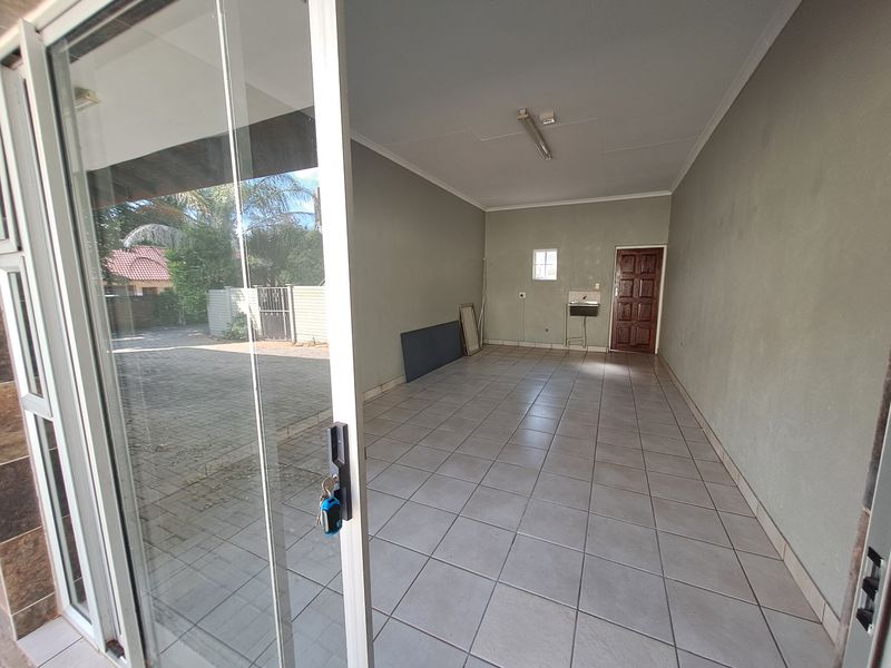 An empty, tiled utility space featuring a utility sink, fluorescent lighting, and direct access to the exterior via a sliding glass door.