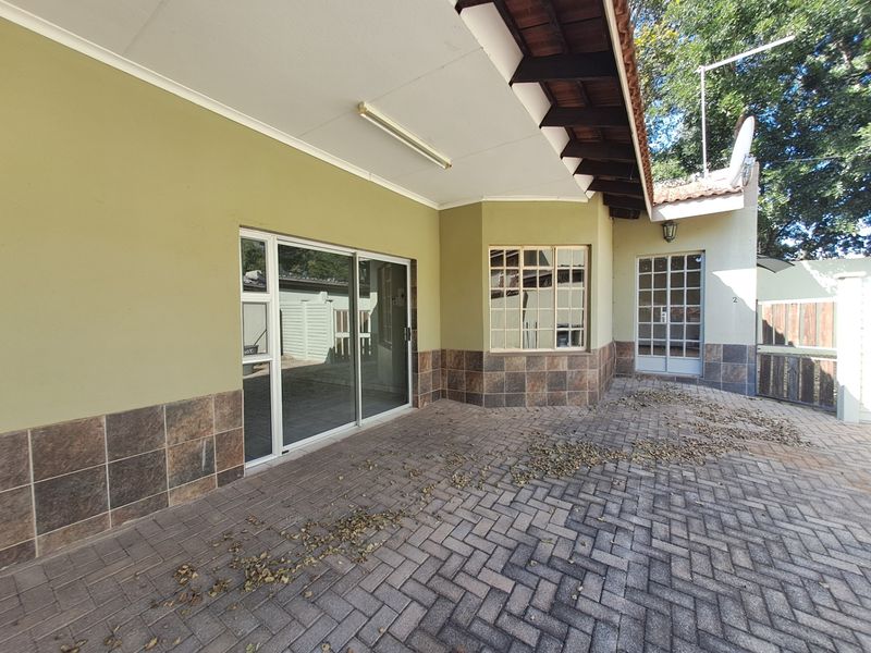 A covered paved patio area featuring sliding glass doors, tiled wall accents, and exposed timber rafters, providing a functional outdoor entertainment space.