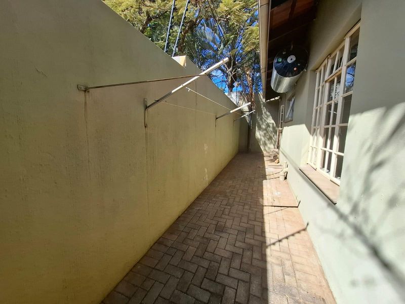 A narrow utility side passage featuring brick paving, a wall-mounted washing line, and an external geyser unit.