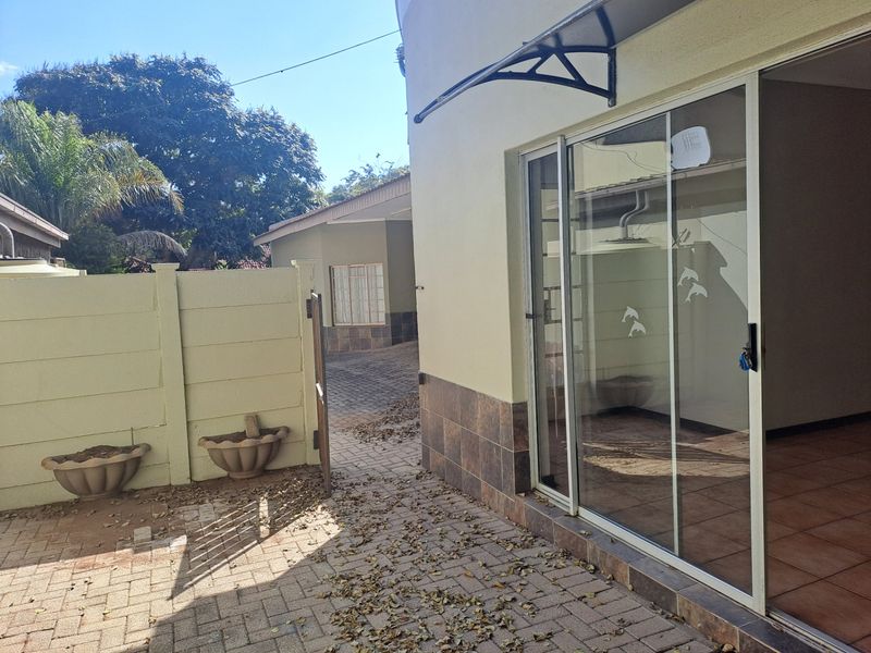 Rear exterior view of the townhouse featuring a paved patio area, sliding glass door access, and a boundary wall.