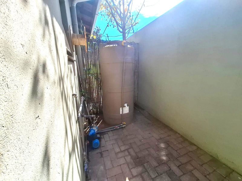 A side utility area featuring a water storage tank and pump system installed on paved ground against a boundary wall.