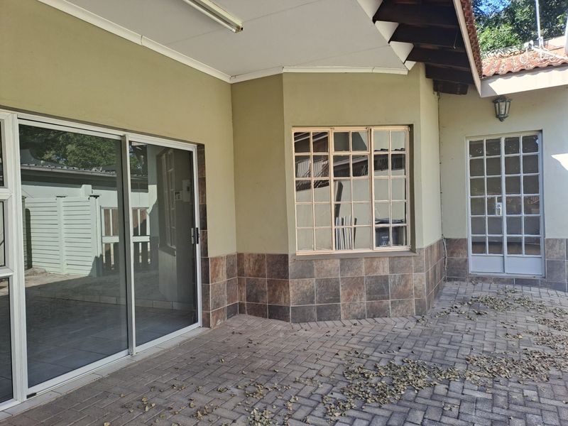 A covered paved patio area featuring tiled wall accents, sliding glass doors, and multi-pane window and door access to the interior.