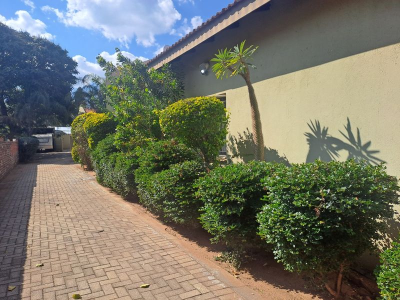 A side view of the townhouse exterior featuring a paved walkway alongside a landscaped garden bed and exterior wall lighting.