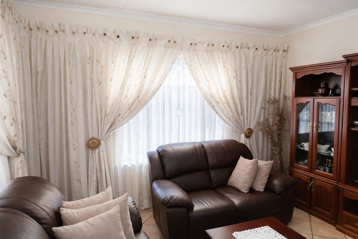 A comfortable living room area featuring tiled flooring and large windows dressed with decorative curtains.