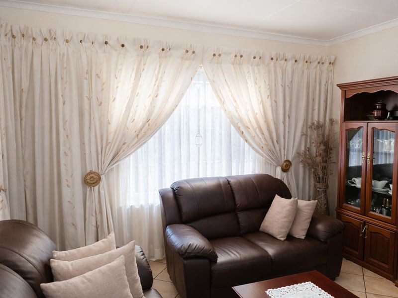A comfortable living room area featuring tiled flooring and large windows dressed with decorative curtains.