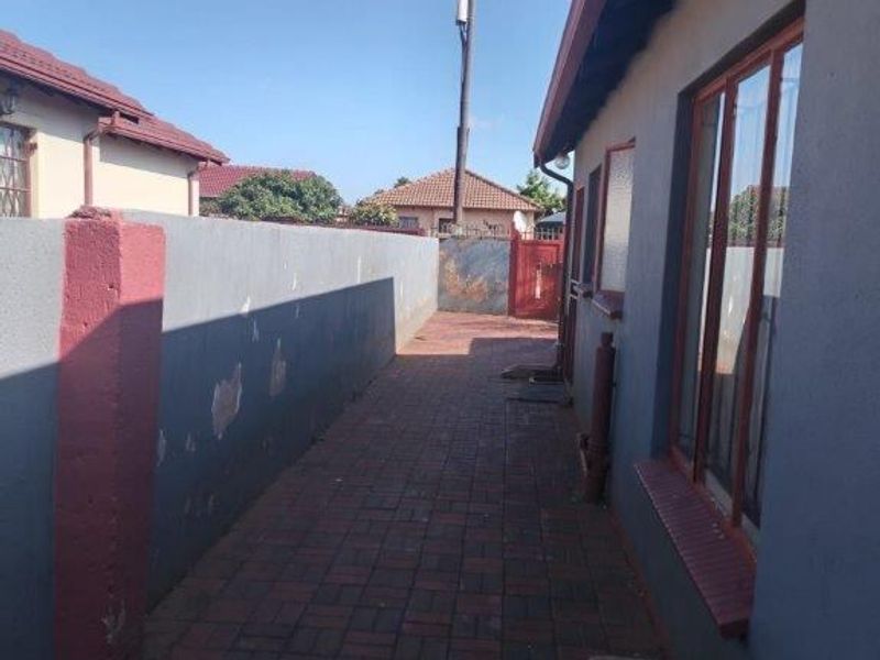 A narrow paved side passage along the exterior of the house, featuring a boundary wall and metal gate access.