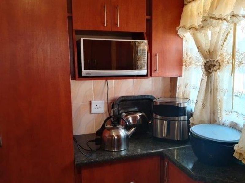 A compact kitchen area featuring warm-toned wooden cabinetry, dark countertops, and a tiled backsplash, providing functional storage and preparation space.