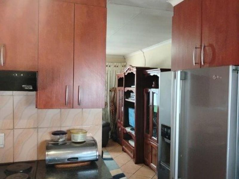 A functional kitchen featuring wood-tone cabinetry, tiled backsplash, and integrated appliances, leading into an adjacent living area with tiled flooring throughout.
