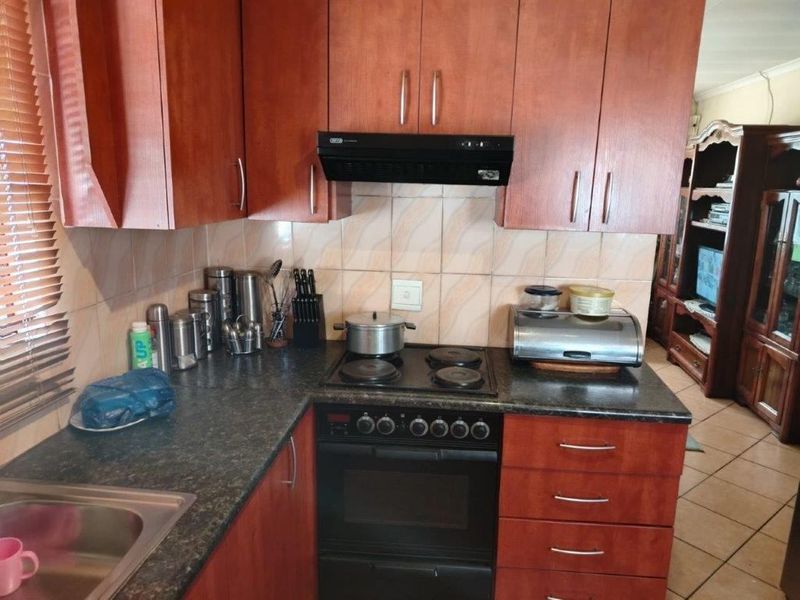 A functional kitchen featuring wood-finish cabinetry, dark laminate countertops, a built-in oven with hob, and a tiled backsplash.
