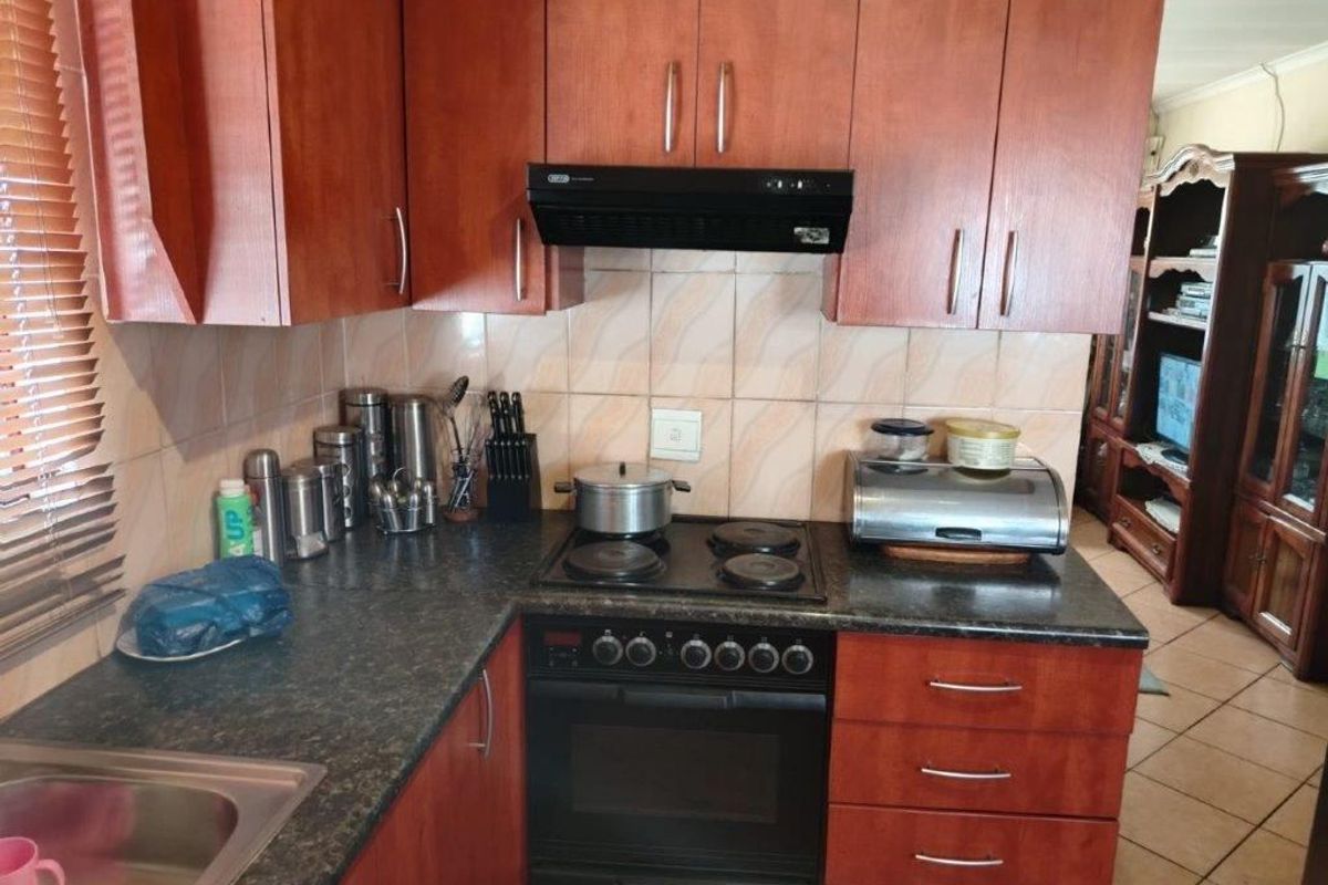 A functional kitchen featuring wood-finish cabinetry, dark laminate countertops, a built-in oven with hob, and a tiled backsplash.