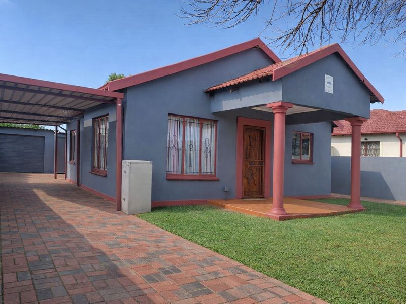 Front view of a well-maintained house featuring a paved driveway, attached carport, detached garage, and a covered entrance porch with decorative columns.