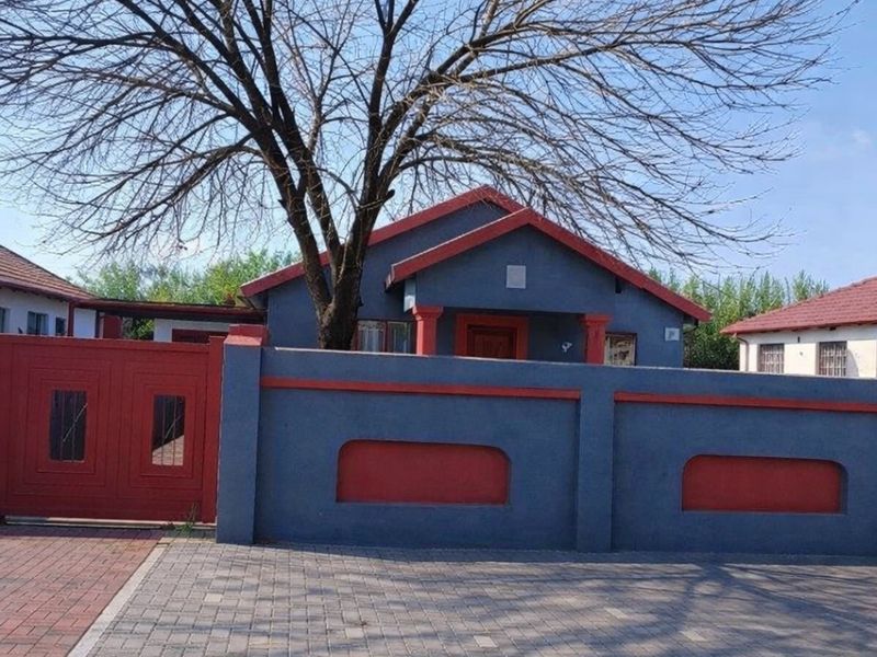 Front view of a residential house featuring a paved driveway, secure boundary wall with a gate, and a covered entrance porch.