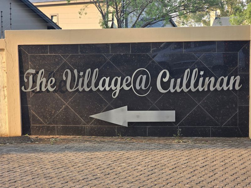 Entrance signage for The Village at Cullinan estate, featuring a stone-clad boundary wall, electric fencing, and paved driveway access.