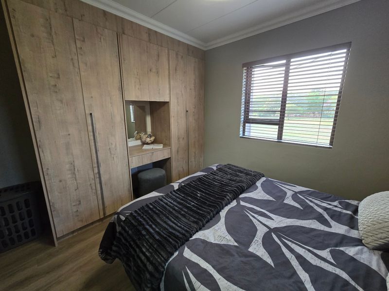 A well-maintained bedroom featuring modern wood-finish built-in cupboards with an integrated vanity and venetian blinds.