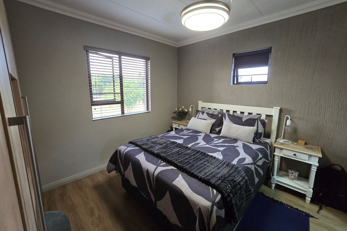 A well-maintained bedroom featuring laminate flooring, a textured feature wall, built-in wardrobe, and dual window treatments for natural light control.