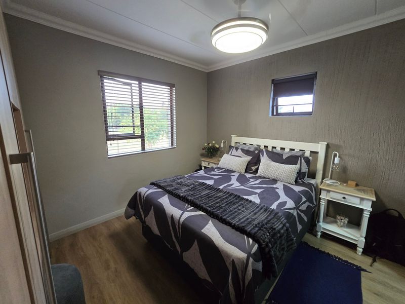 A well-maintained bedroom featuring laminate flooring, a textured feature wall, built-in wardrobe, and dual window treatments for natural light control.