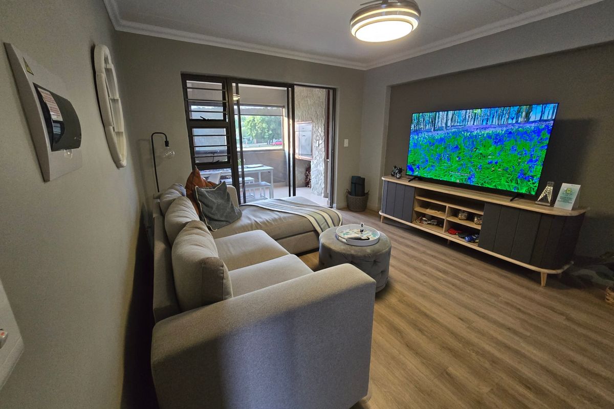 A well-maintained living room featuring laminate flooring, cove molding, and sliding glass doors that provide access to an outdoor patio area.