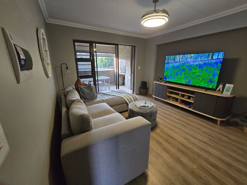 A well-maintained living room featuring laminate flooring, cove molding, and sliding glass doors that provide access to an outdoor patio area.
